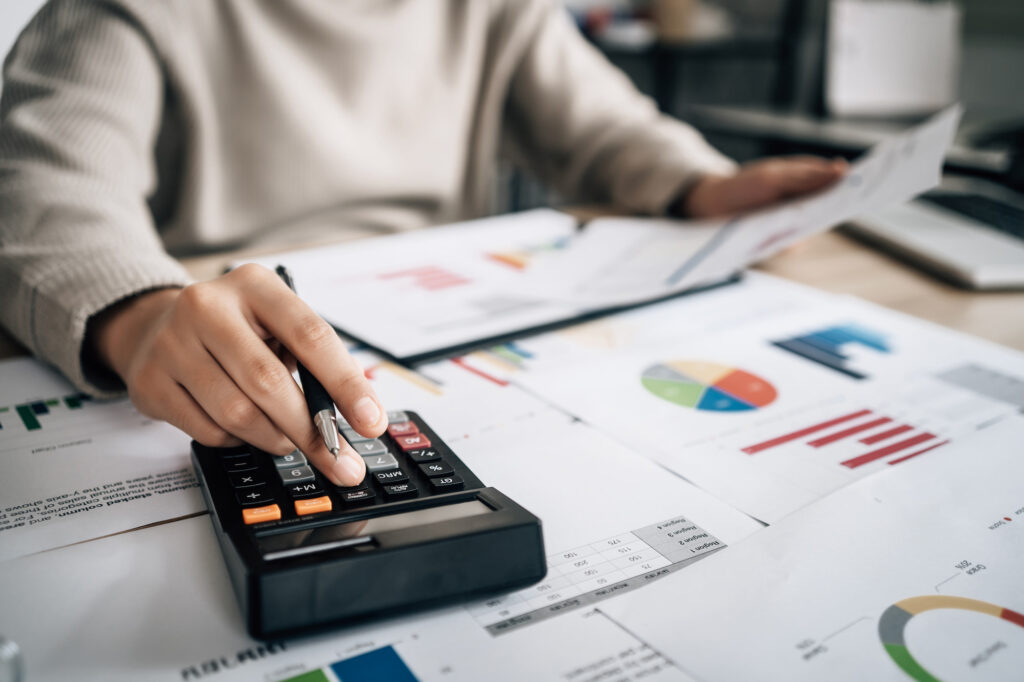 A person uses a calculator and reviews documents with charts and graphs on a desk, highlighting cost analysis and financial planning essential for effective business budgeting.